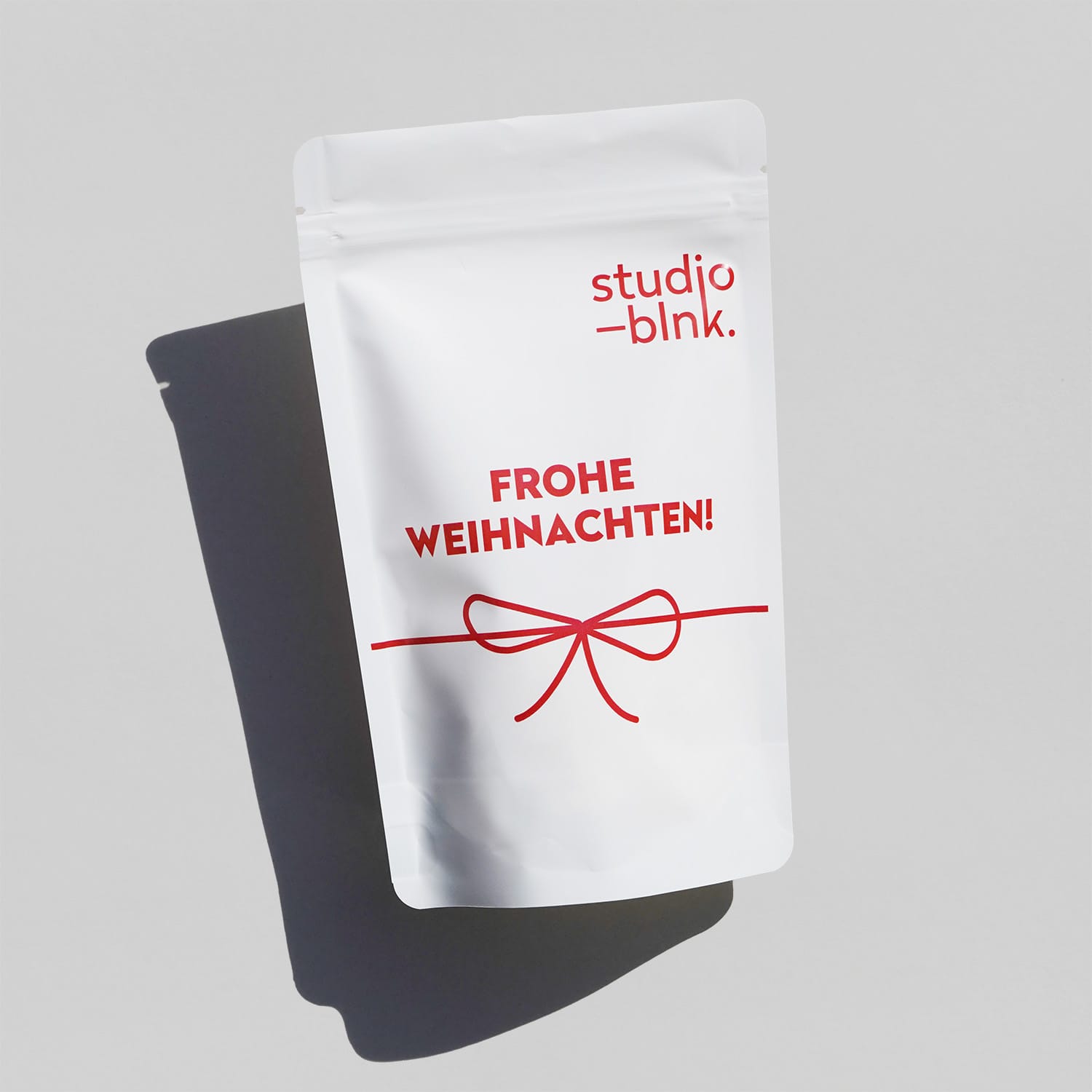 Eine weiße PET Tüte für dragierte Produkte mit roter Schrift. 'Frohe Weihnachten, ein Muster Logo und eine große Schleife.