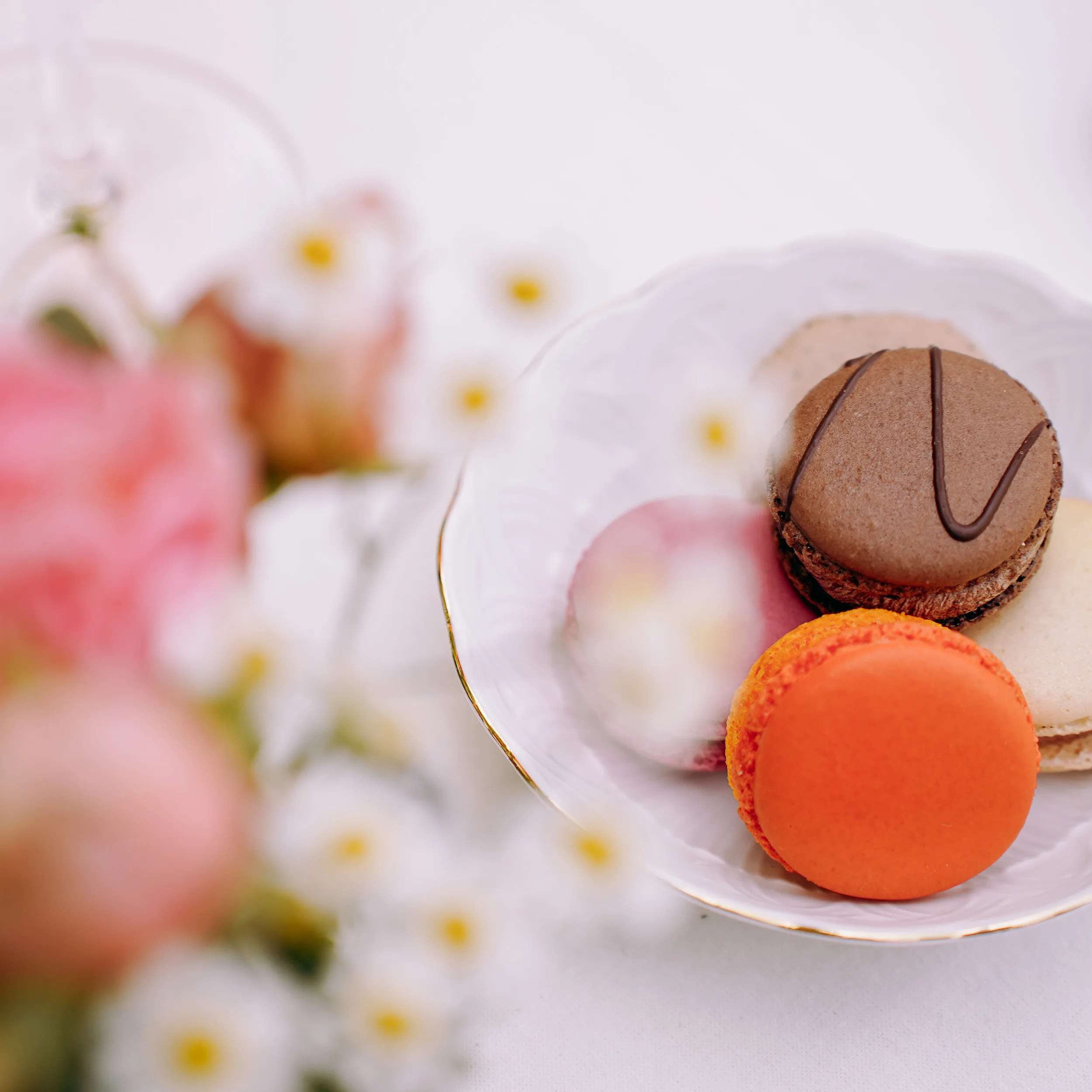 fünf Macarons in einer weißen Porzellanschale. Im Vordergrund ein unscharfer Blumenstrauß auf einer Hochzeitstafel