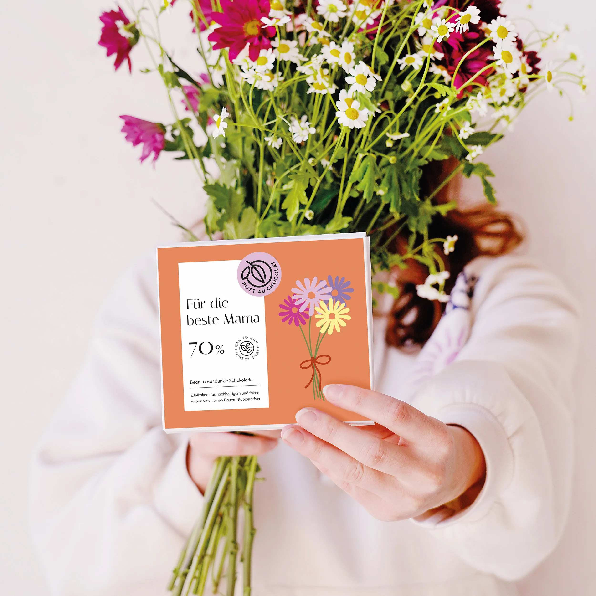 Frau hält einen bunten Frühlings Blumenstrauß vor ihr Gesicht in der anderen Hand streckt sie unsere dunkle Tafelschokolade 