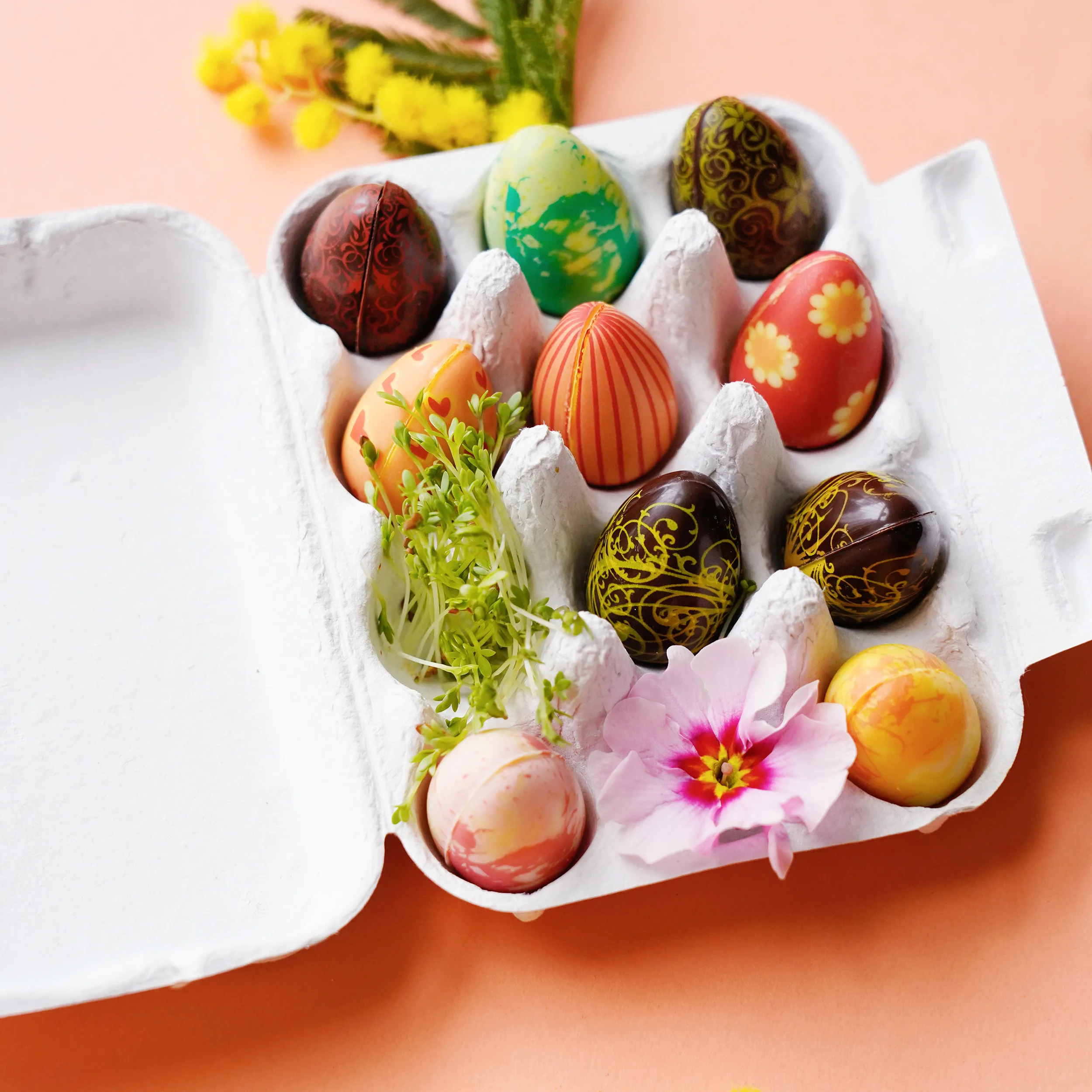 Geöffnete Verpackung von Schokoladen-Ostereiern von Pott au Chocolat: Natürlicher Karton, ähnlich einem echten Eierkarton, nur kleiner. Darin bunte Schokoladen-Ostereier mit verschiedenen Mustern wie Streifen, Blumen, Punkten und mehr