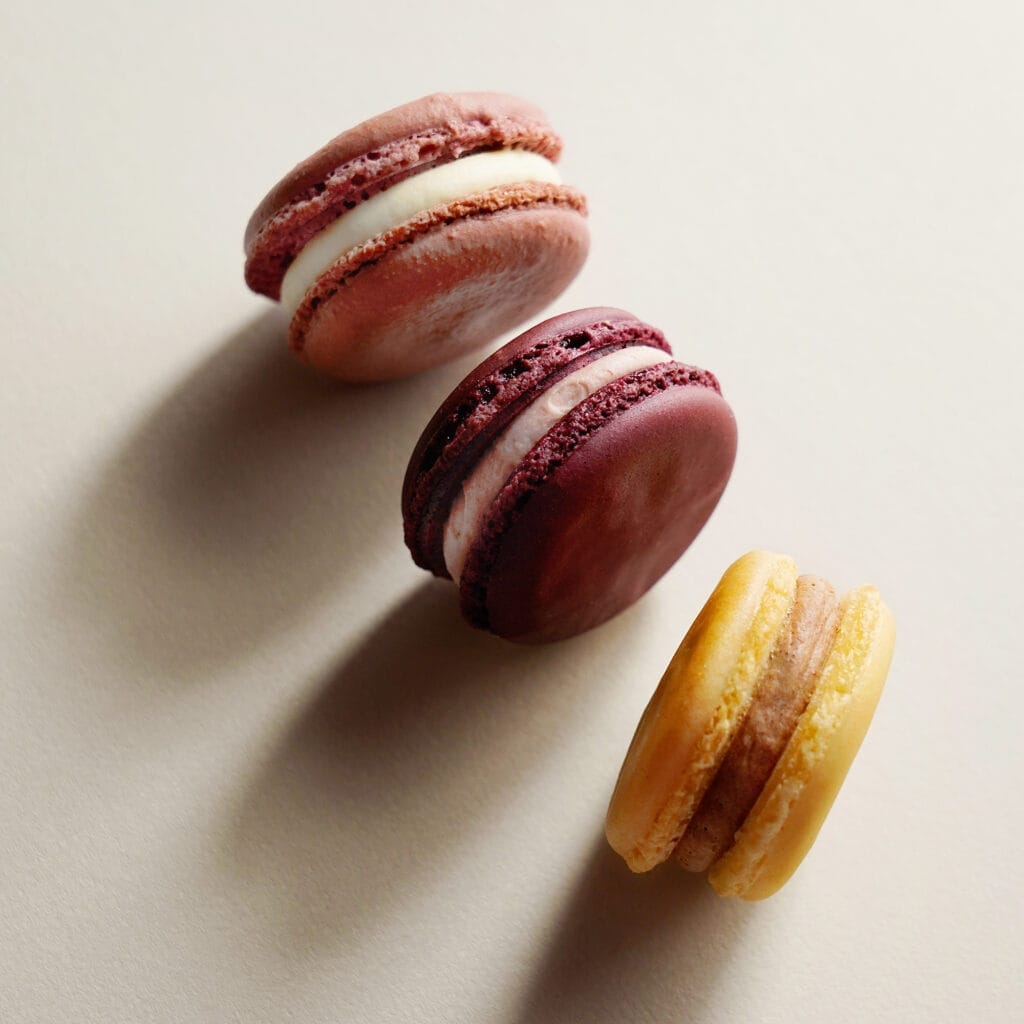 Drei Macarons in einem Rosa-, Gelb- und Beerenton von oben fotografiert.