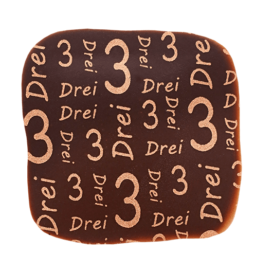 Eckige Praline mit dunkler Schokolade überzogen und mit einem Kupferfarbenen Print mit der Zahl und dem Wort drei