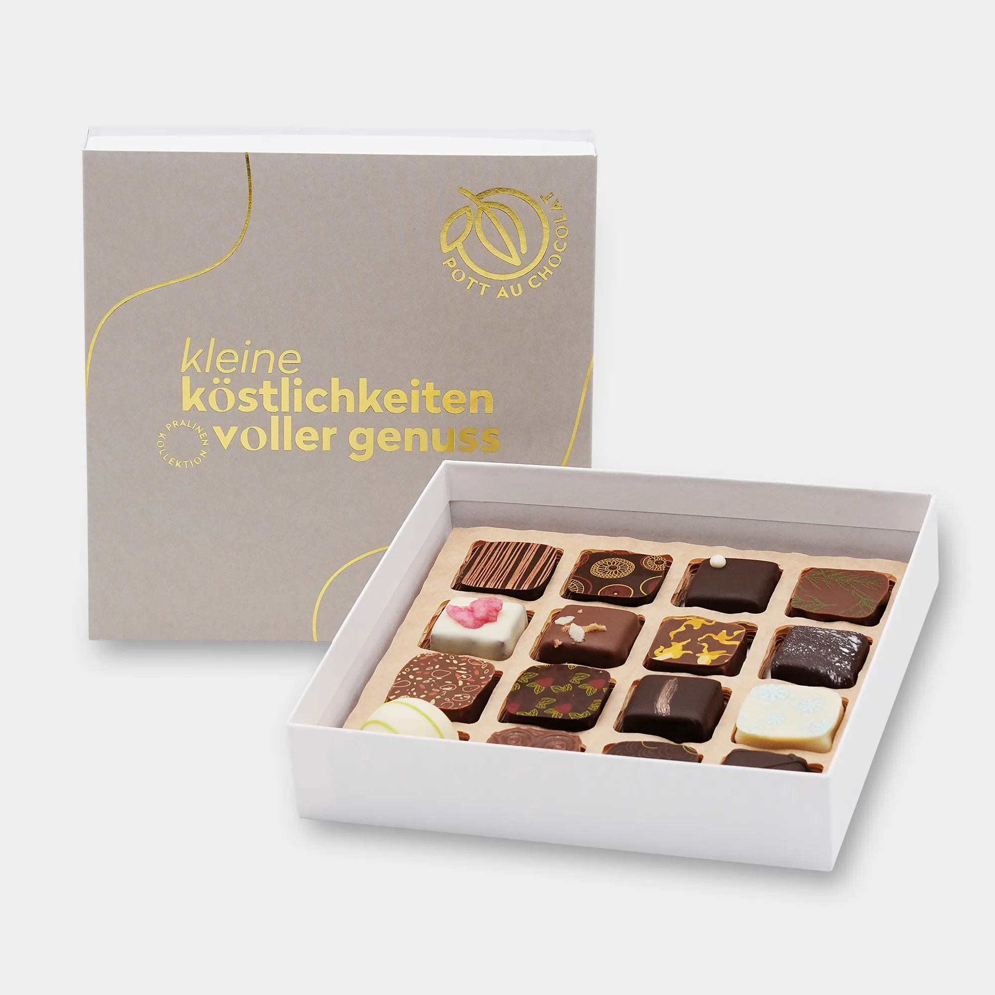 Aufgestellte schlichte Pralinenbox in Grau mit goldgeprägter Schrift: 'Kleine Köstlichkeiten voller Genuss'. Davor eine offene Box mit bunt gemischten Pralinen