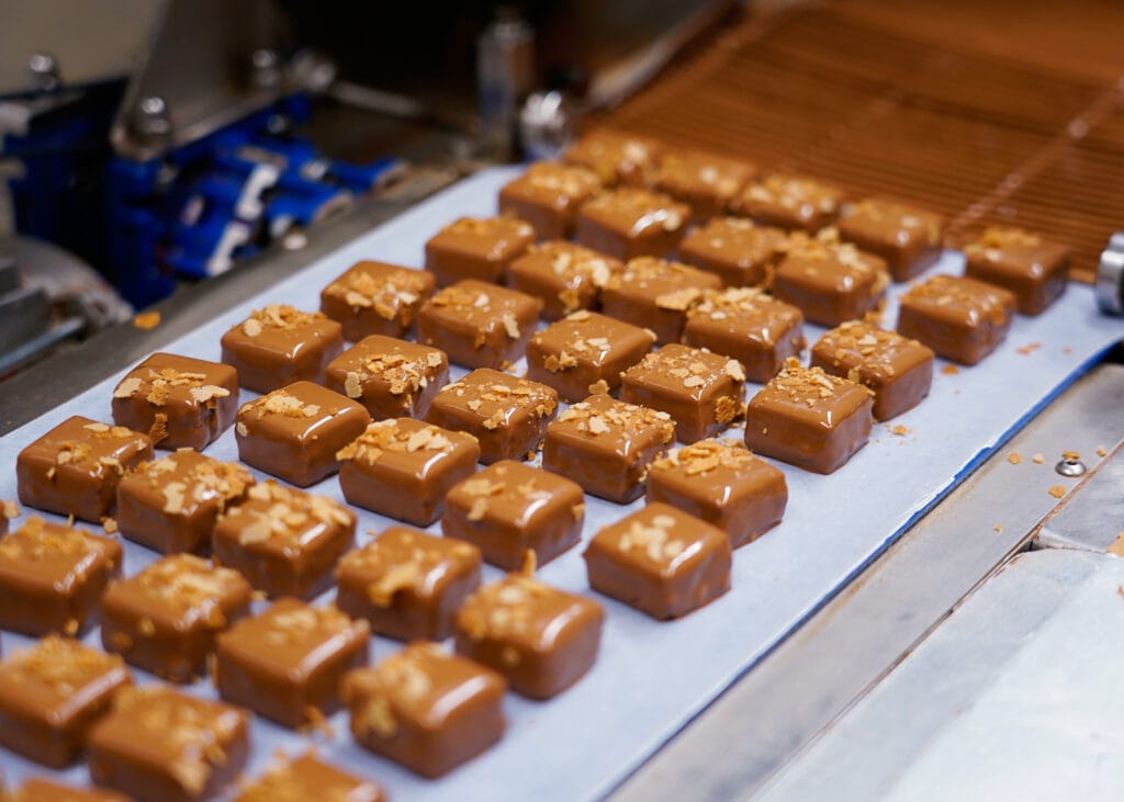 In der Produktion: Frisch mit Schokolade überzogene Pralinen werden mit Feuilletines verziert.