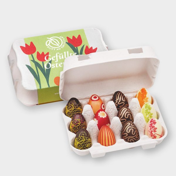 Ostereierkarton mit 12 bunten Schokoladen-Ostereiern. Dahinter der geschlossene Karton mit grüner Banderole und bunten Blumen.
