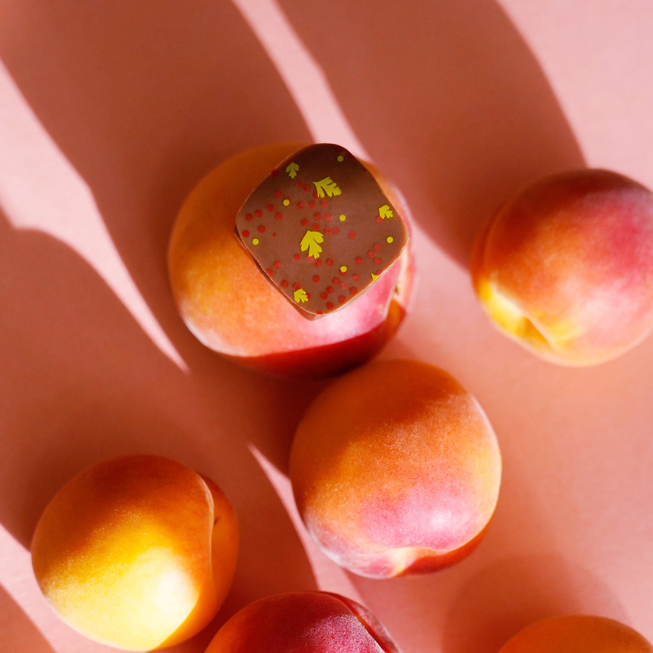 Eine Praline mit Rot grünen Verzierungen auf einem Rosa Orangenem Hintergrund mit Pfirsichen