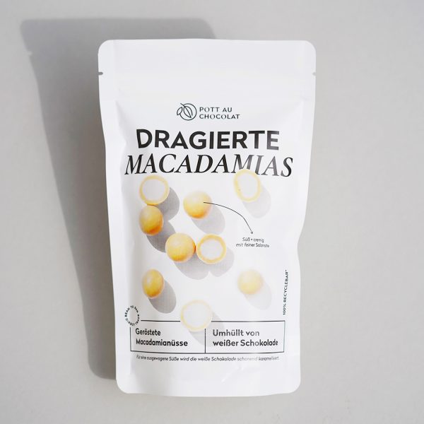 Schokolierte Macadamia Nüsse in. weißer PET Tüte mit Aufdruck. Man sieht die dragierten Macadamias, teilweise aufgeschnitten und umhüllt von Blonder Schokolade.