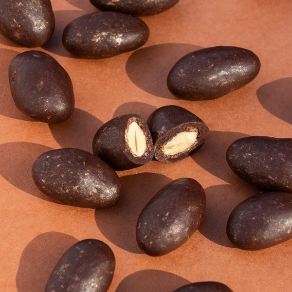 Karamellisierte Mandeln in dunkler Schokolade auf braunem Hintergrund. Eine Mandel ist angeschnitten.