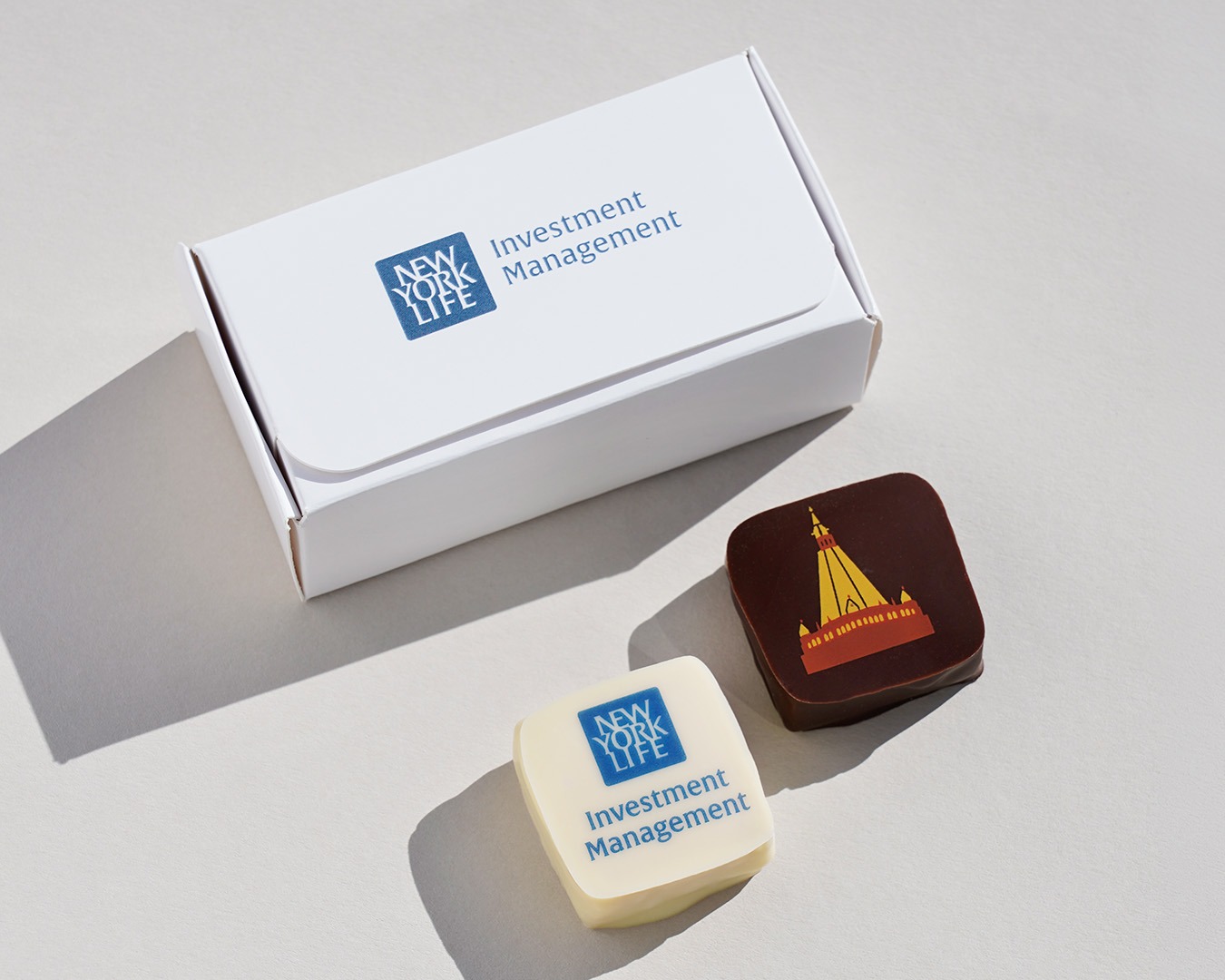 Beispiel von mit Logo bedruckten Pralinen und eigener gestalteter Verpackung. 
Zwei Pralinen und eine weiße Schachtel.