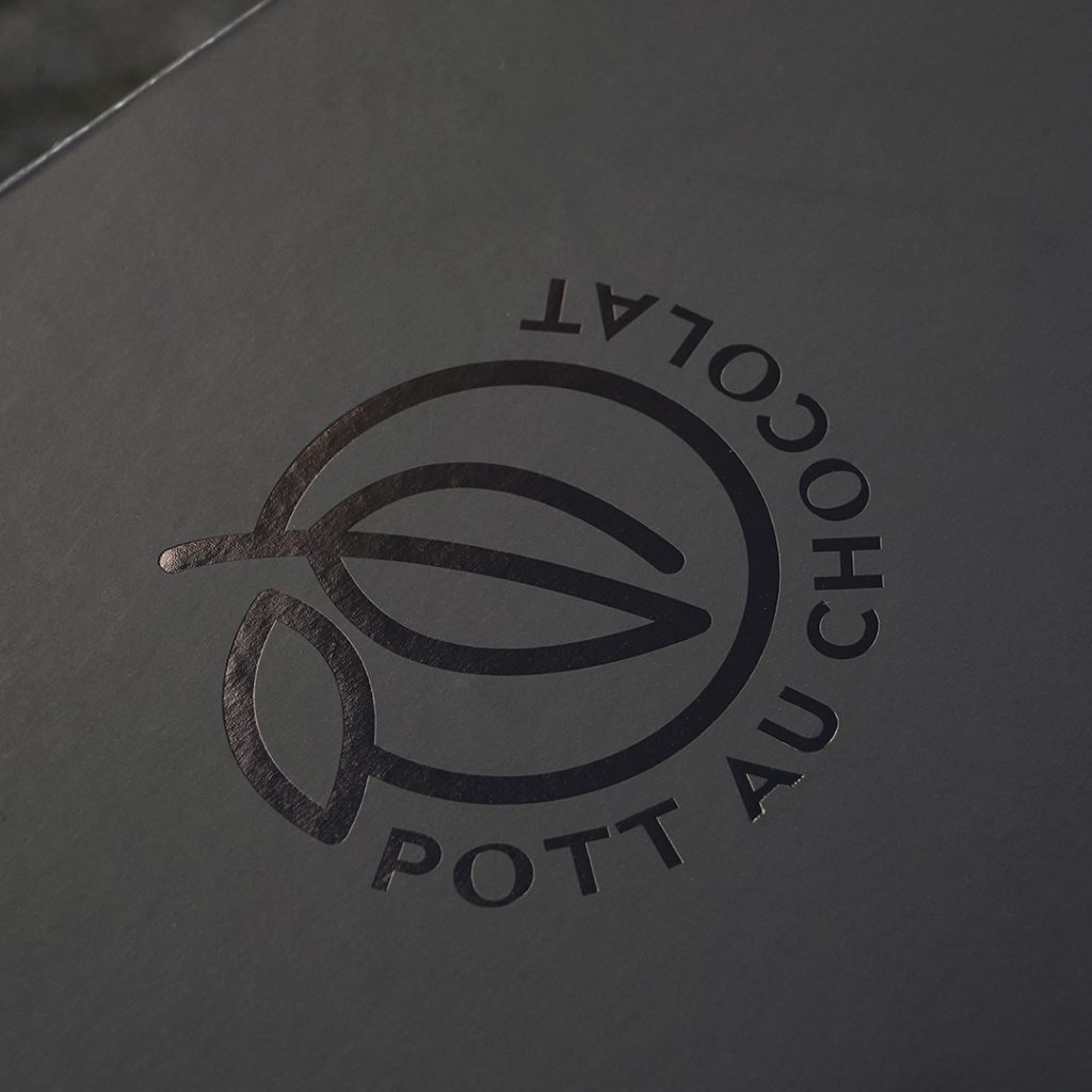 Detail des geprägten Logos von Pott au Chocolat auf der Oberseite der schwarzen Geschenkbox. Das Logo ist schwarz geprägt mit leichtem Glanz.