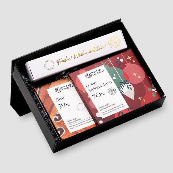 Schwarze Geschenkbox mit einer Stange mit 6 Pralinen mit weißer Banderole mit gold geprägtem 'Frohe Weihnachten'. Zusätzlich zwei Tafeln. Zimt 39% und 'Frohe Weihnachten' 70% im weihnachtlichen Design in Rot, Grün und Weiß.