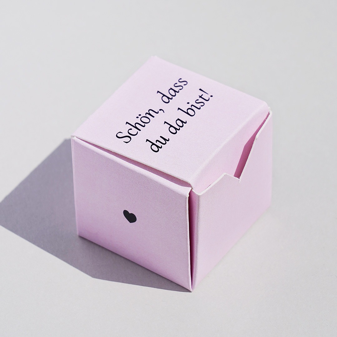Kleine Schachtel in Würfelform in rosa mit schwarzem Herz und Schrift 'Schön, dass du da bist!'