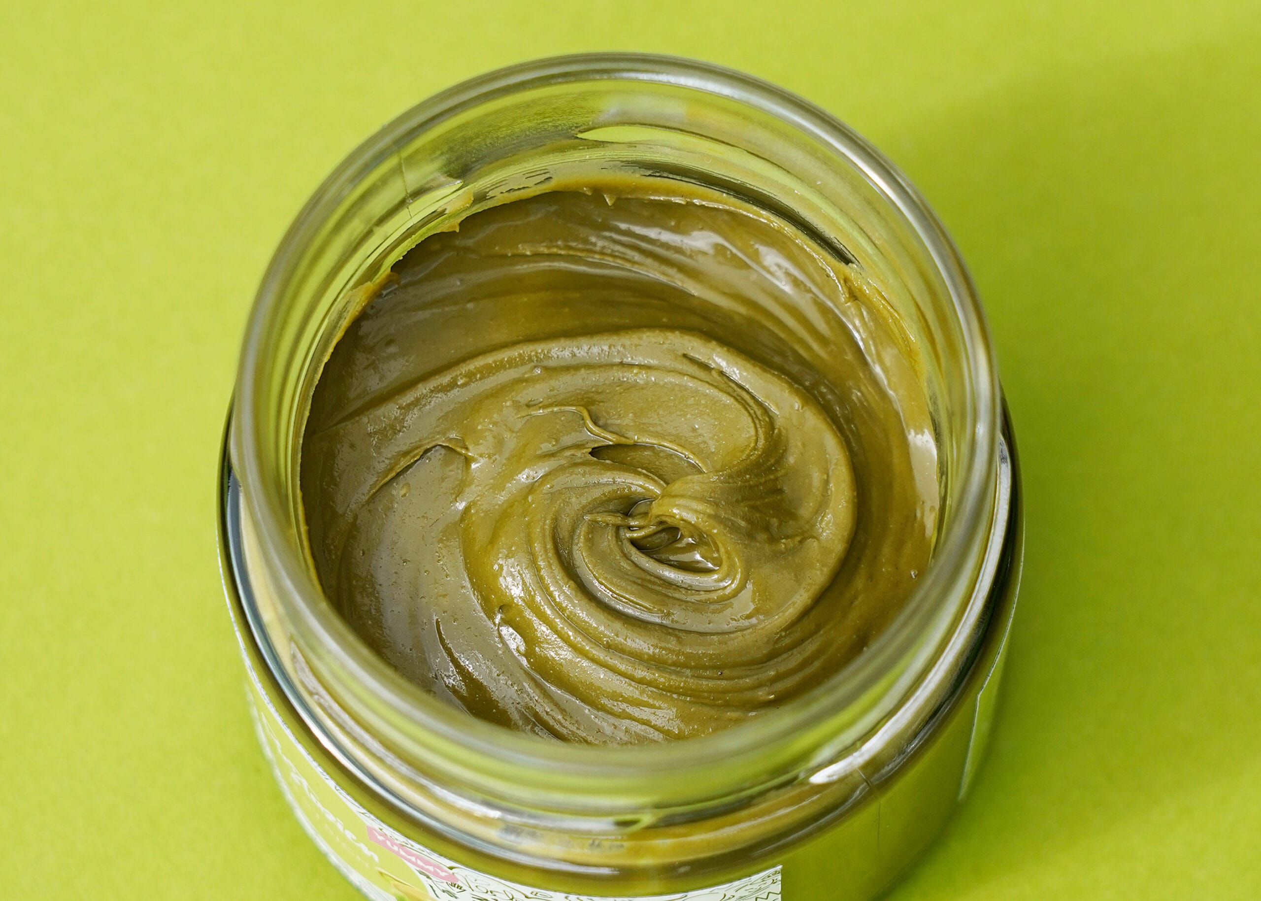 offenes Glas mit Pistazien-Aufstrich von oben fotografiert auf grünem Untergrund