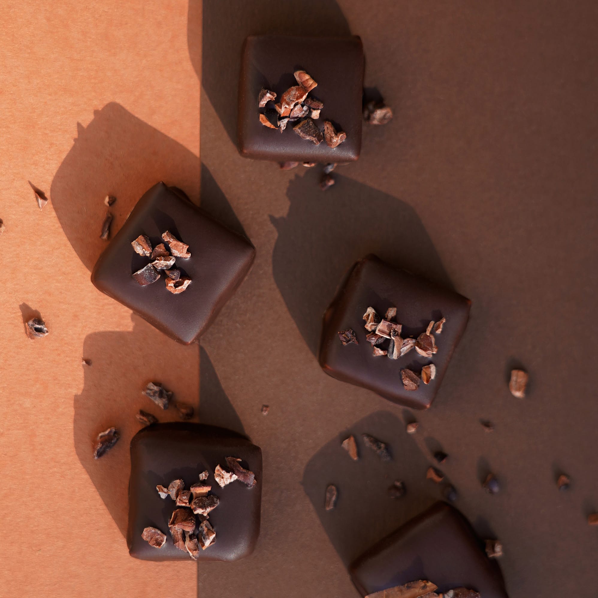Dunkel überzogene Nougat-Kakaosplitter-Praline mit Kakaosplittern on top auf einem braunen Hintergrund mit verstreuten Kakaosplittern