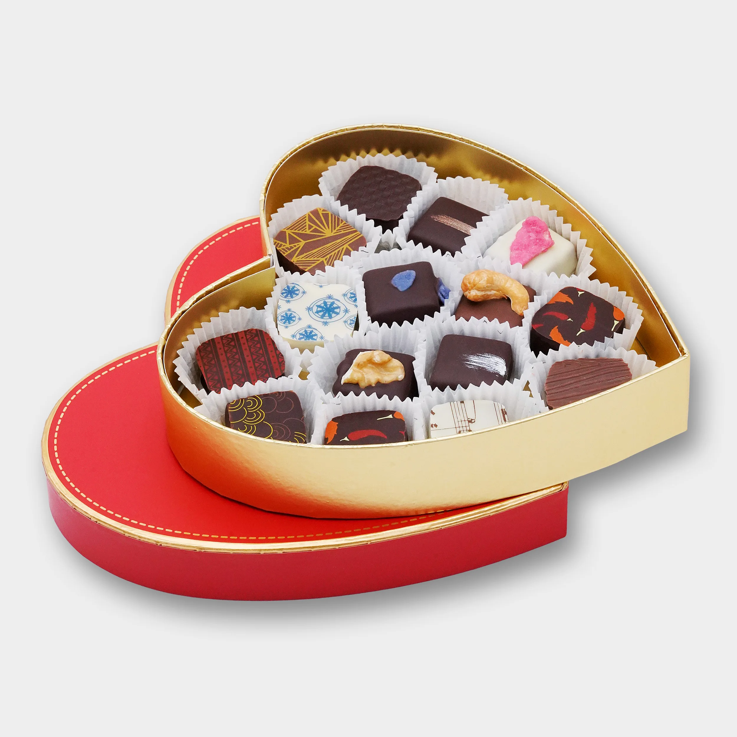 Pralinen in einer goldenen Box mit rotem Deckel in Herzform. Die geöffnete Schachtel liegt auf dem Deckel