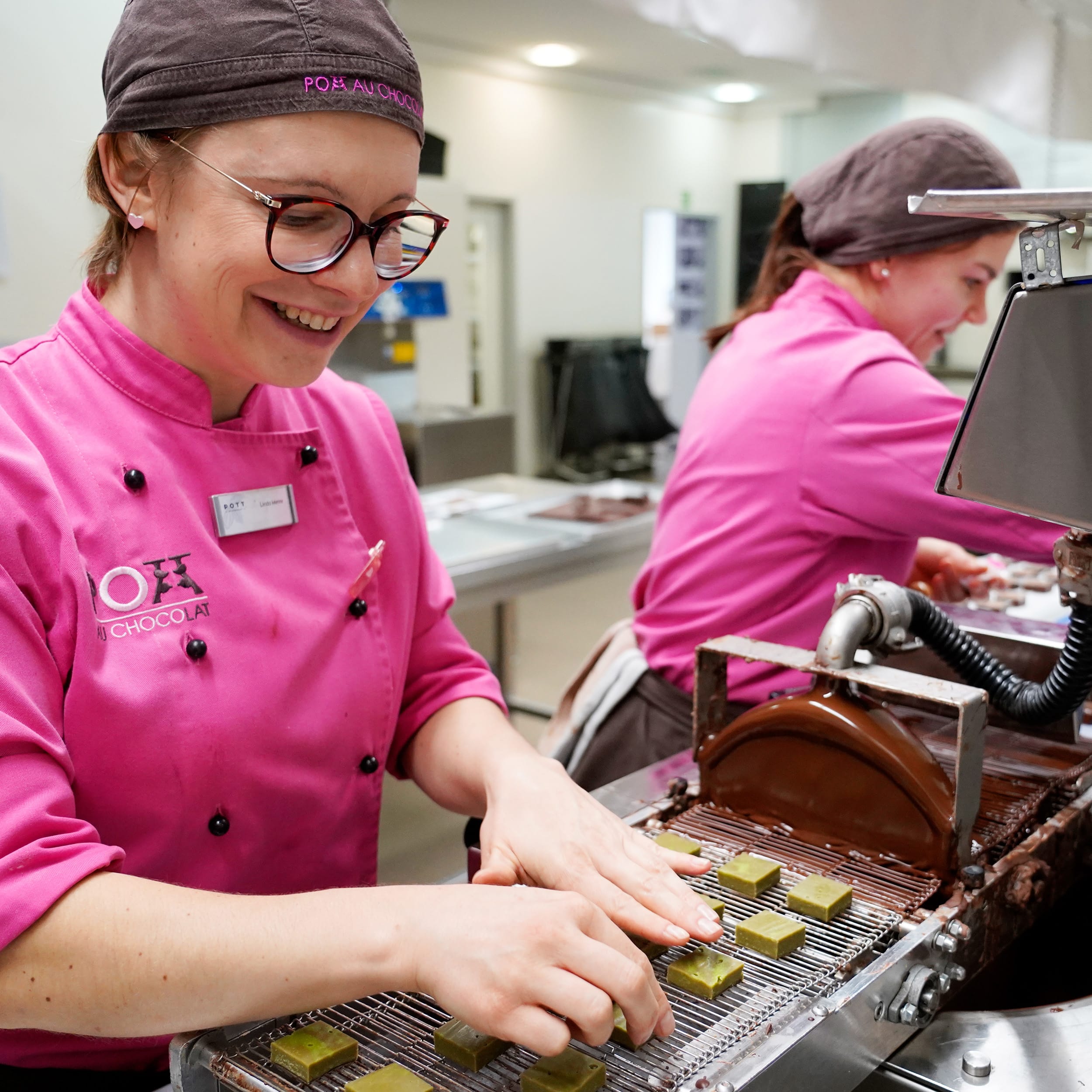 Das Produktionsteam von Pott au Chocolat überzieht Pralinen mit Schokolade.