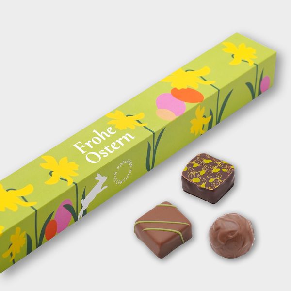 Detail der 10er Pralinen-Stange im Oster-Design mit Hase, Eiern und Narzissen. Davor liegen drei Pralinen als Beispiel