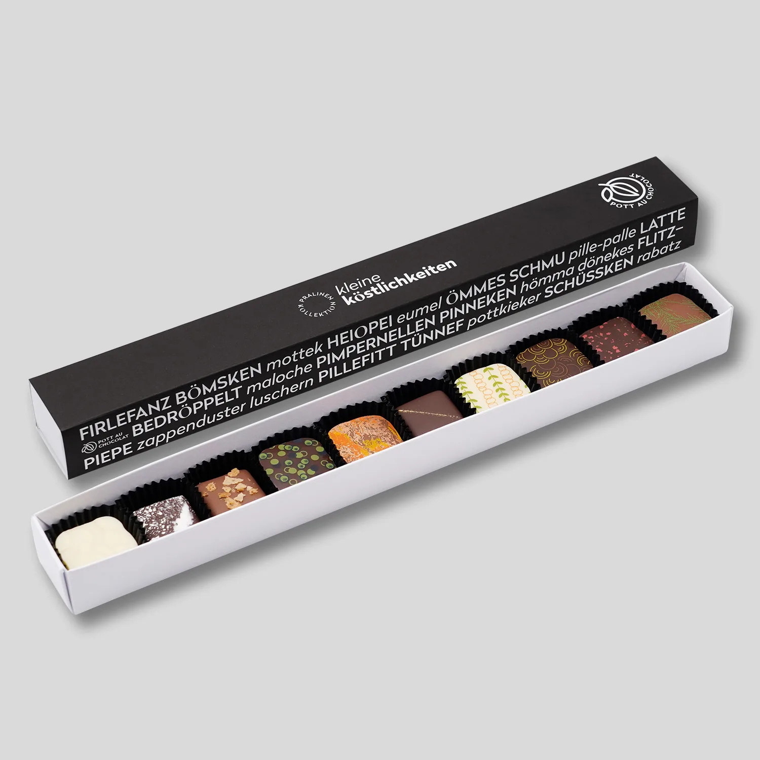 Pralinenstange mit 10 bunt dekorierten Pralinen. Die Banderole ist schwarz mit weißer Schrift. Darauf steht 'Kleine Köstlichkeiten' und verschiedene Wörter, die typisch für das Ruhrgebiet sind. Firlefanz, Bömsken, hömma...