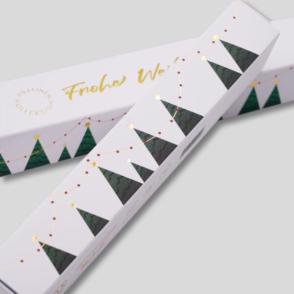 Details der Pralinenstangen in weiß mit Weihnachtsmotiv. In gold geprägt 'Frohe Weihnachten' und Bäumchen mit Lichterkette.