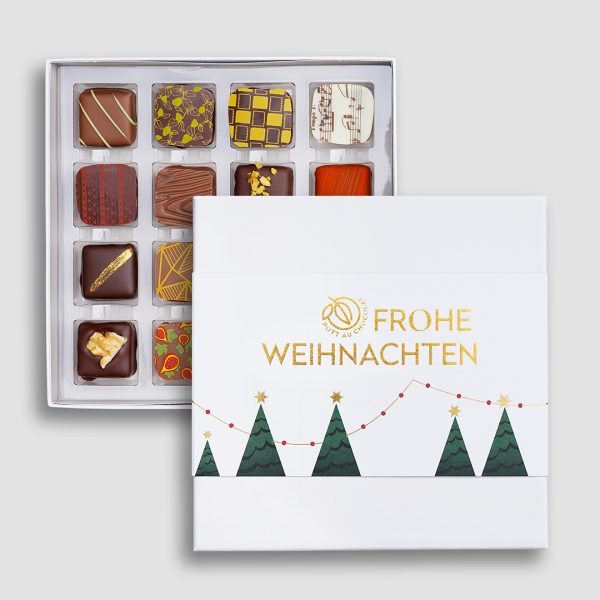 Weiße Pralinenbox mit Banderole mit Aufschrift 'Frohe Weihnachten' in gold geprägt mit Tannenbäumen. Darunter die geöffnete Verpackung mit bunt dekorierten Pralinen.