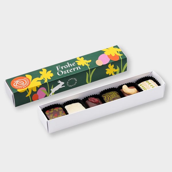 Geöffnete Pralinenstange mit 6 bunt dekorierten Pralinen. Dahinter die geschlossene Stange mit Banderole in dunkelgrün mit Illustrationen: Narzissen, Hase und bunte Eier und Aufschrift: Frohe Ostern