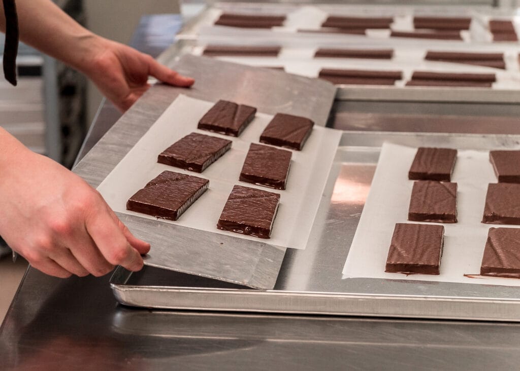 Frisch mit Schokolade überzogene Tafeln werden in der Produktion auf ein Tablett gelegt. Im Hintergrund sind weitere Tafeln zu sehen