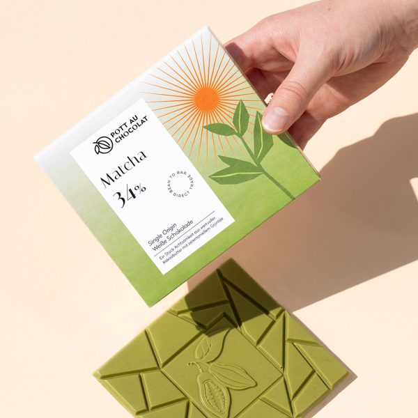 Weiße Matcha Schokolade Verpackung von einer Hand gehalten, daneben die ausgepackte grüne Schokoladentafel.