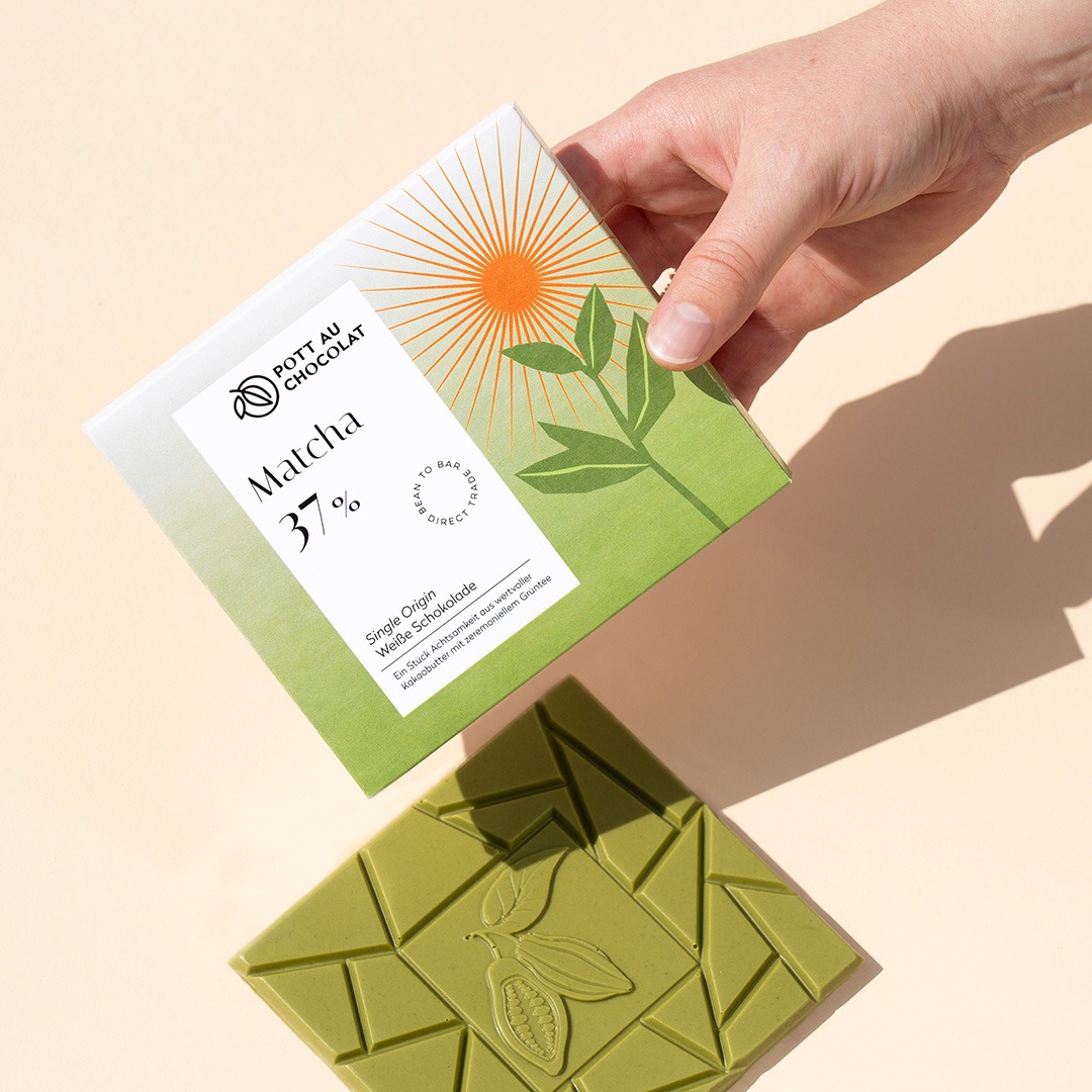 Weiße Matcha Schokolade Verpackung von einer Hand gehalten, daneben die ausgepackte grüne Schokoladentafel.