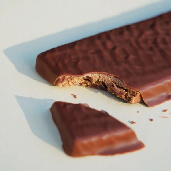 Tafel gefüllt mit Nougat und Kakaosplittern in Milchschokolade. Eine Ecke ist abgebrochen, dass man die Füllung sehen kann.
