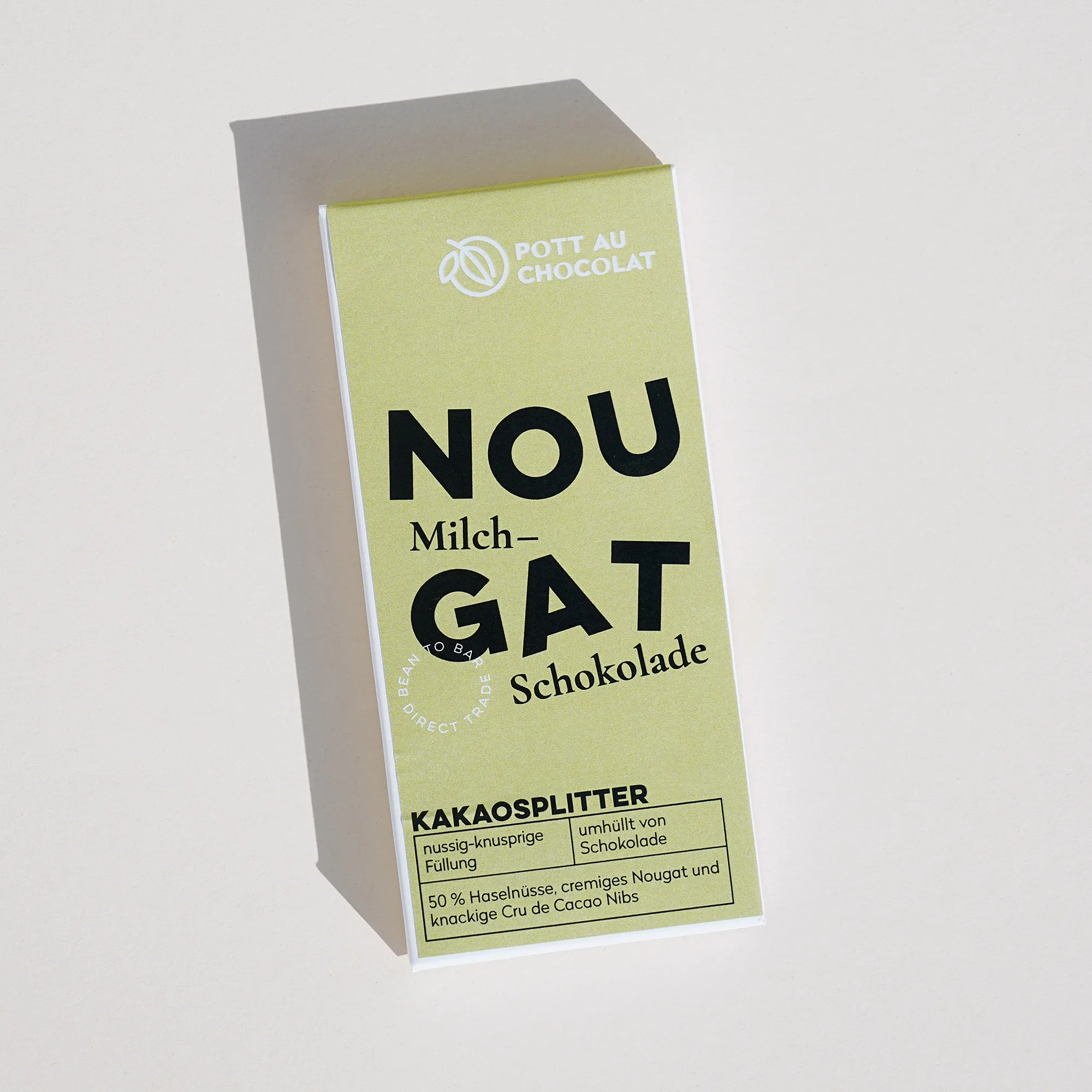 Gefüllte Tafel aus Milchschokolade in Verpackung mit der Aufschrift 'Nougat Kakaosplitter'. Die Aufschrift ist verspielt mit tanzenden Buchstaben gestaltet. Farben des Designs: Hellgrün, Schwarz und Weiß