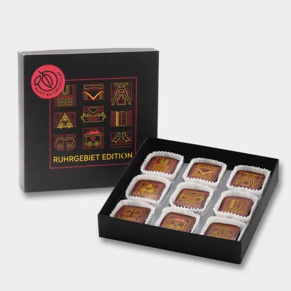 Schwarze Pralinenbox im Ruhrgebiet-Design. Eine Box aufgestellt, davor eine geöffnete Pralinenbox mit Pralinen, mit Ruhrpott-Motiven