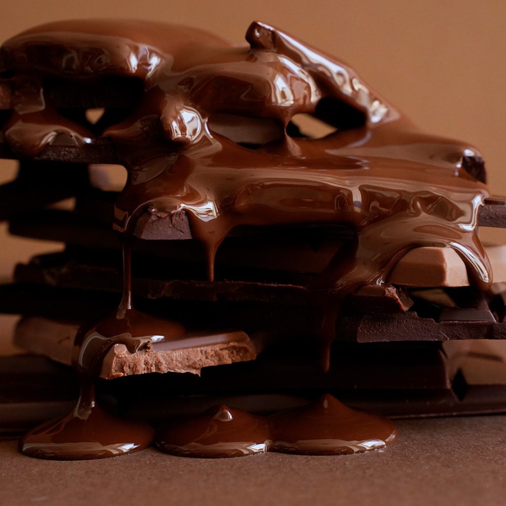 Ein Stapel mit verschiedenen Schokoladentafeln wird mit flüssiger Schokolade übergossen