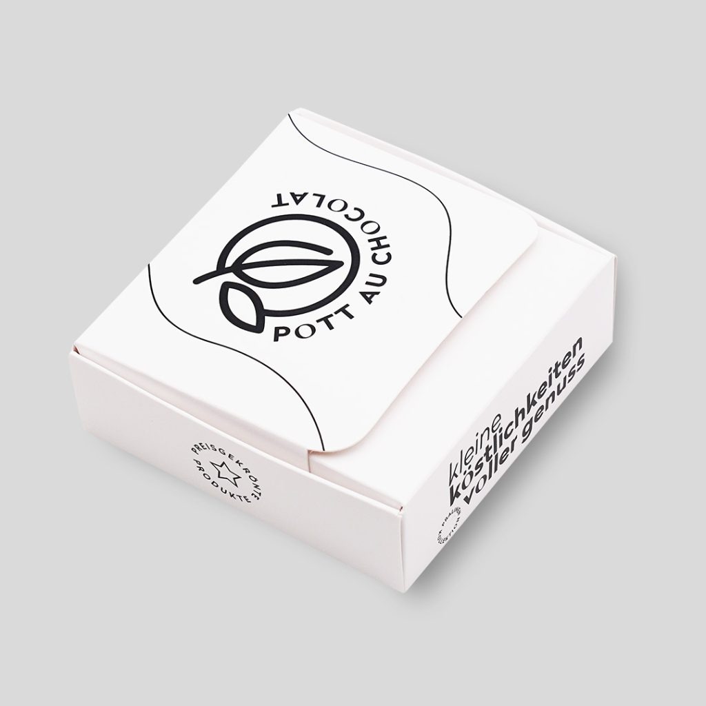 Kleine Box aus weißem Karton mit schwarzer Schrift: 'Kleine Köstlichkeiten voller Genuss', 'Preisgekrönte Produkte' und das Logo von Pott au Chocolat