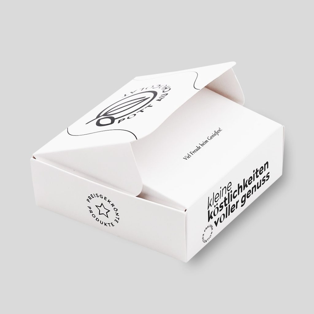 Kleine halb geöffnete Box aus weißem Karton mit schwarzer Schrift: 'kleine Köstlichkeiten voller Genuss', 'Preisgekrönte Produkte', 'Viel Freude beim Genießen' und das Logo von Pott au Chocolat