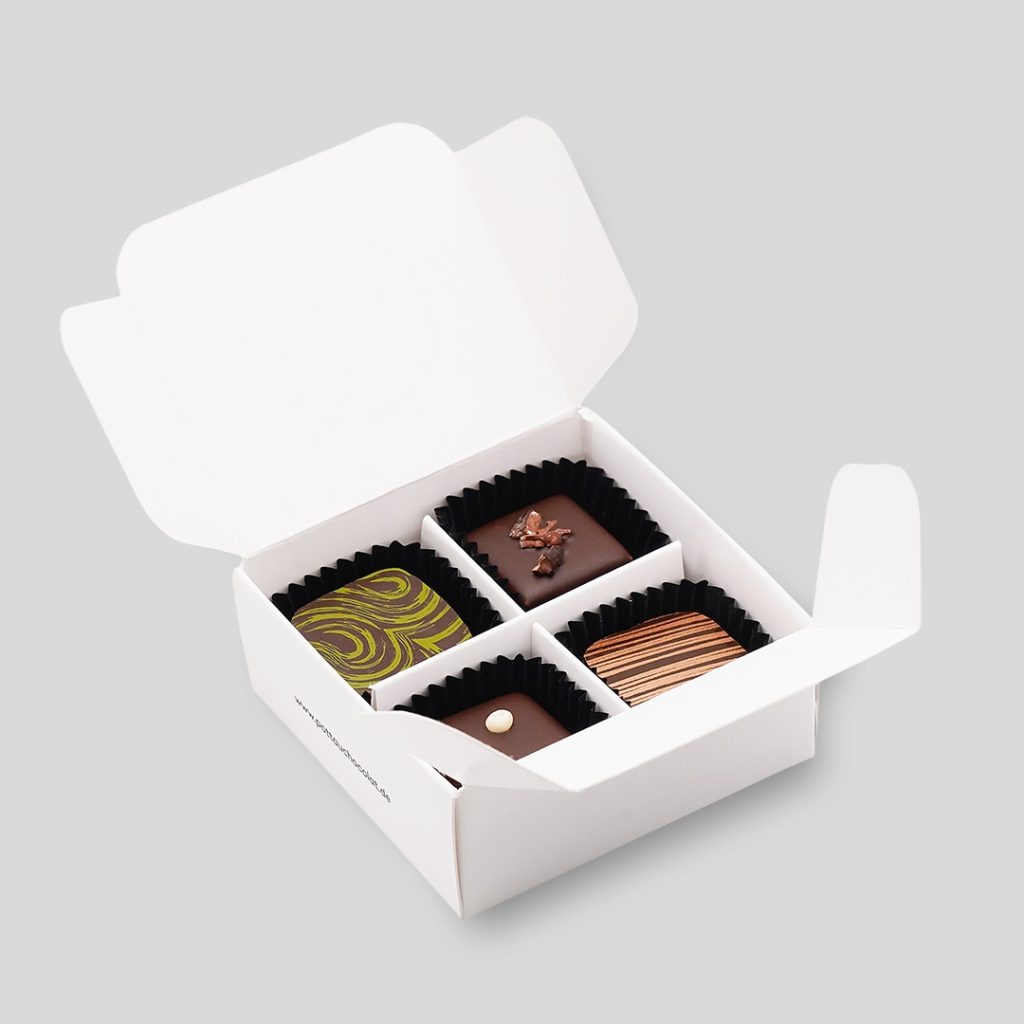 4er Pralinen Schachtel aus weißem Karton geöffnet mit 4 bunt dekorierten Pralinen in schwarzen Papier Kapseln.