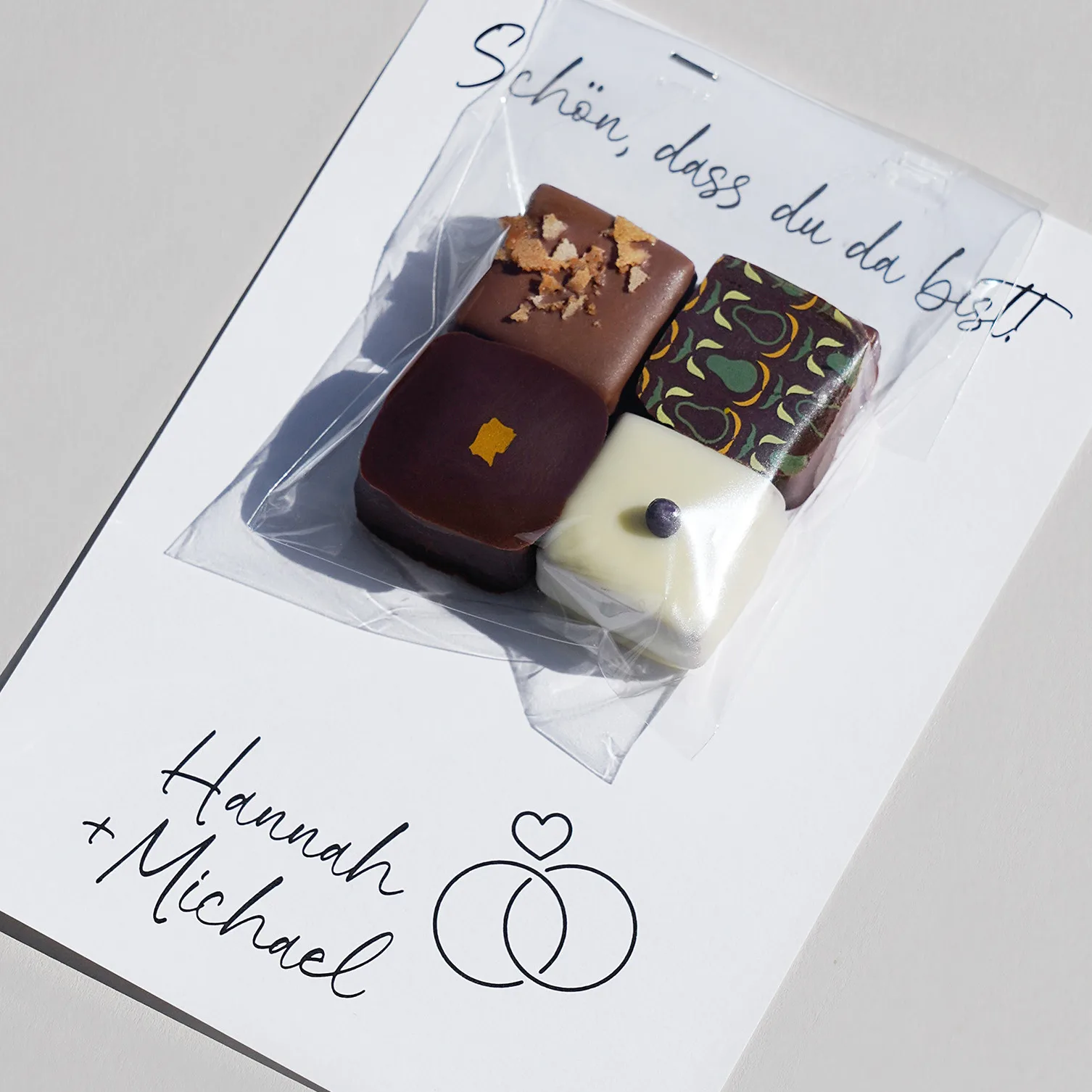 Vier Pralinen in transparenter Tüte, die an eine Beispiel Hochzeitskarte angetackert sind.