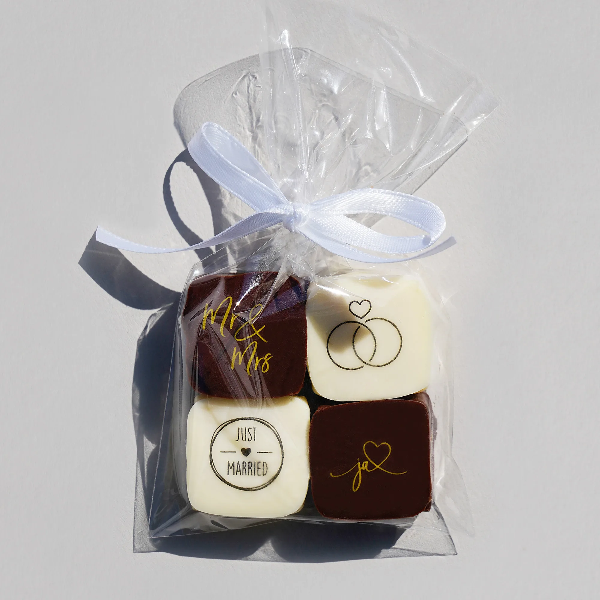 Vier Pralinen mit Hochzeitsaufdrucken (2 in dunkler und 2 in weisser Schokolade) verpackt in transparentem Tütchen mit einer weissen Schleife