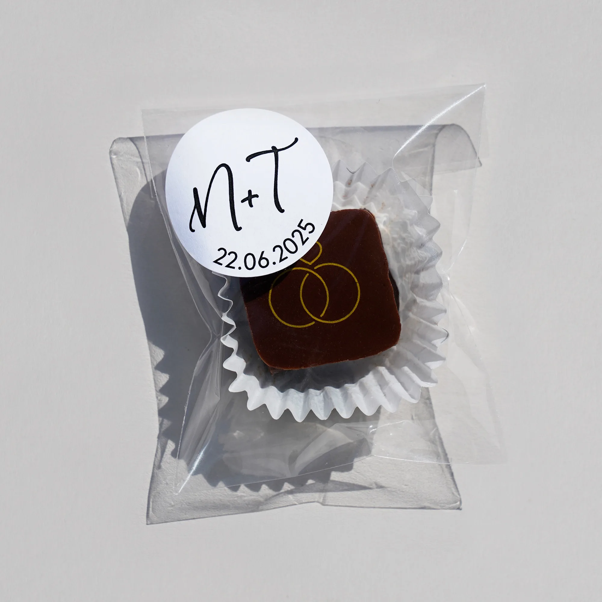 eine Praline im Tütchen mit dunklem Überzug und einem Aufdruck aus unserer Hochzeitspralinen Kollektion versehen mit einem individualisierten runden Etikett
