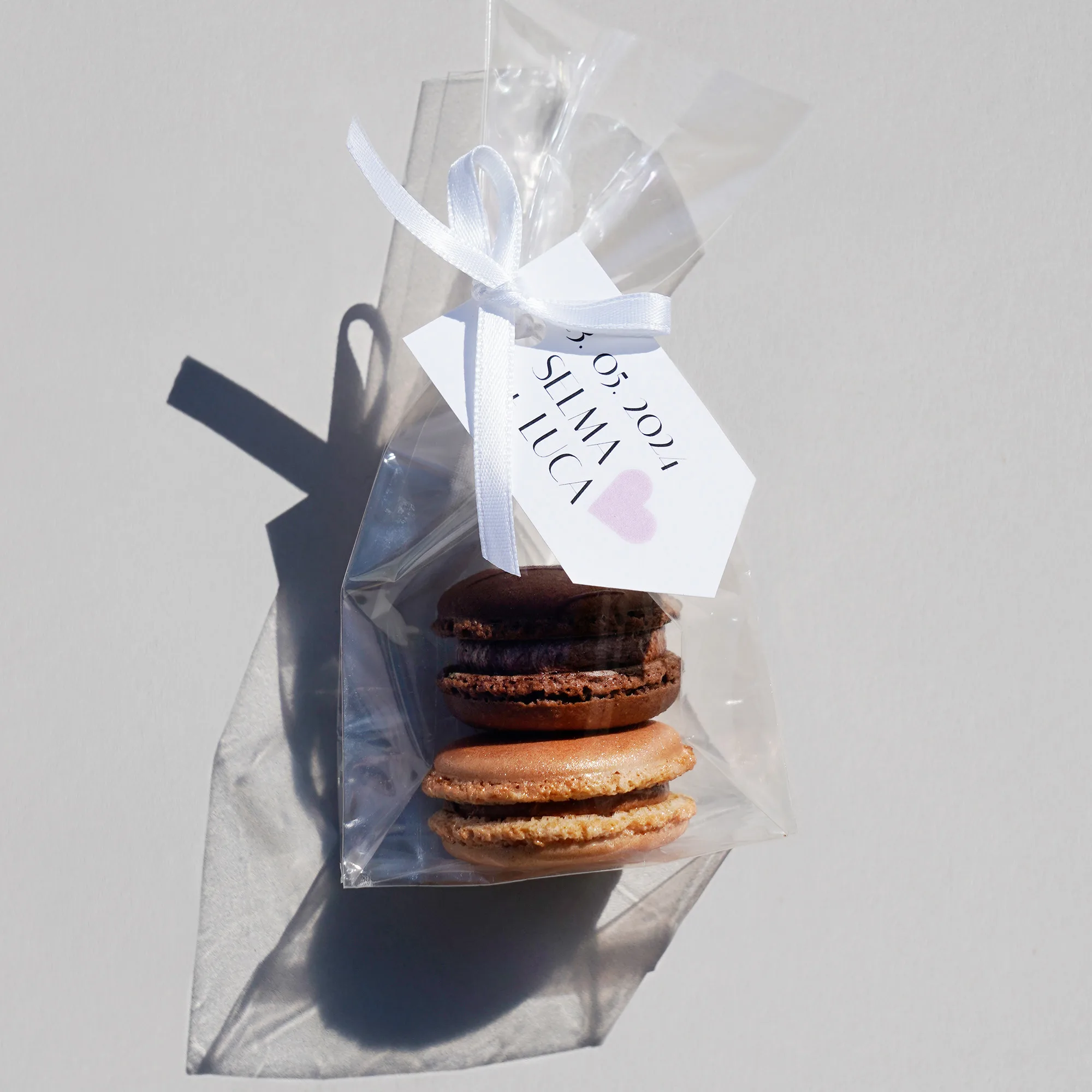 zwei Macarons in einem transparenten Tütchen mit weisser Schleife und Anhänger