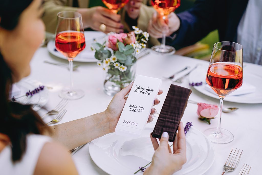 Eine Person sitzt am gedeckten Hochzeitstisch und hält eine Tafel Schokolade und die personalisierte Verpackung dazu in der Hand.