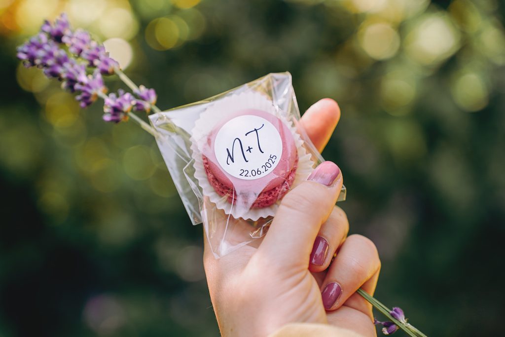 Macaron in transparentem Tütchen in einer Hand. Auf dem Tütchen ist ein weißer Sticker mit 'M+T' und einem Datu.