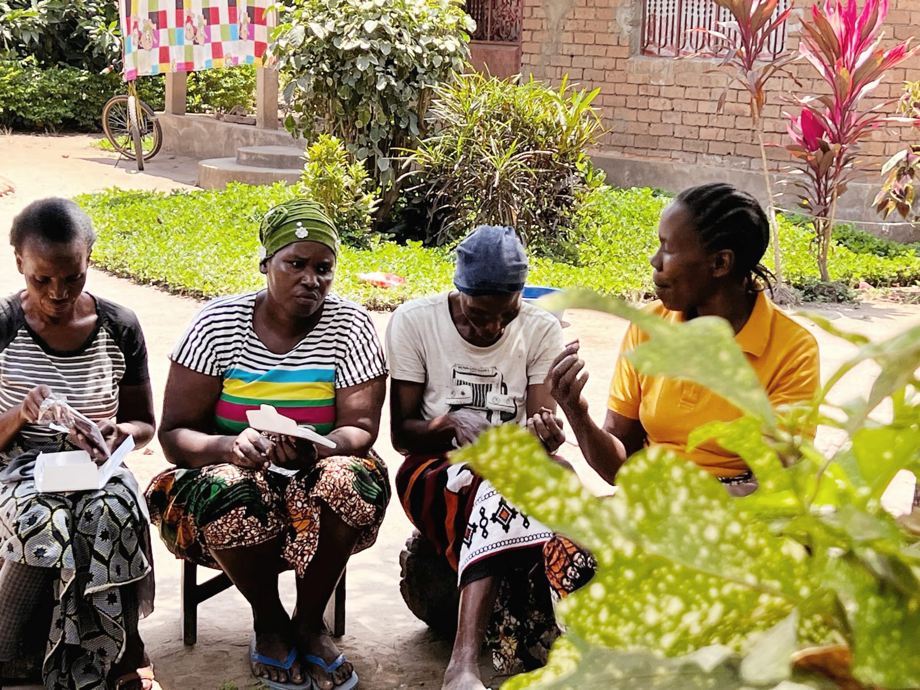 Vier Kakaobäuerinnen in Tansania vor ihrem Backsteinhaus beim Verkosten von mitgebrachter Tafelschokolade von Pott au Chocolat
