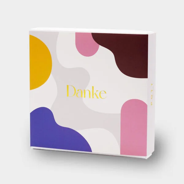Aufgestellte Pralinenbox "Danke" von Vorne: bunte organischen Formen mit der goldgeprägten Aufschrift 'Danke'.