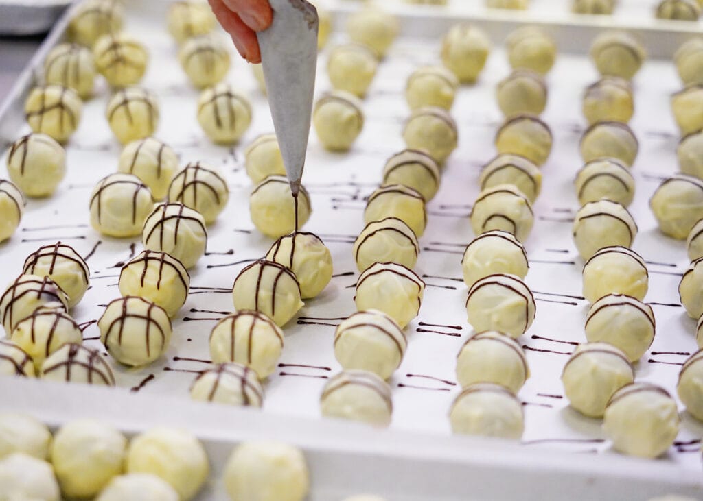 In der Produktion: Pralinen mit weißem Schokoladenüberzug werden mit dunkler Schokolade verziert.