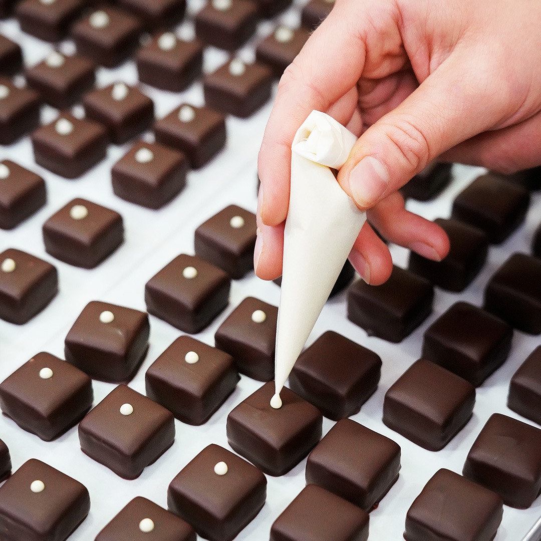 Pralinen werden dekoriert in der Produktion. Sie bekommen einen weißen Punkt aus Schokolade