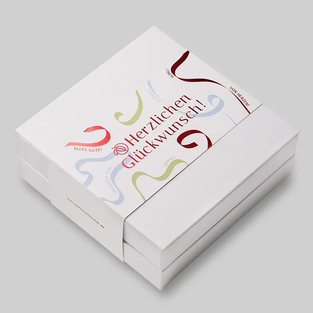 Doppelstöckige quadratische Pralinen Schachtel mit 'Herzlichen Glückwunsch' Motiv mit Luftschlangen in rot, blau und grün. Der Hintergrund des Motivs ist weiß, die rote Schrift ist geprägt und schimmert metallisch.