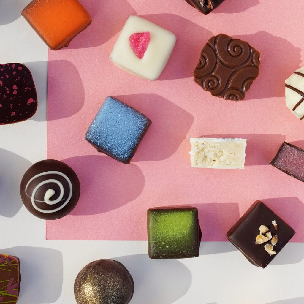 Verschiedene Sorten Pralinen von Pott au Chocolat angeordnet auf farbigem Untergrund, einige davon angeschnitten