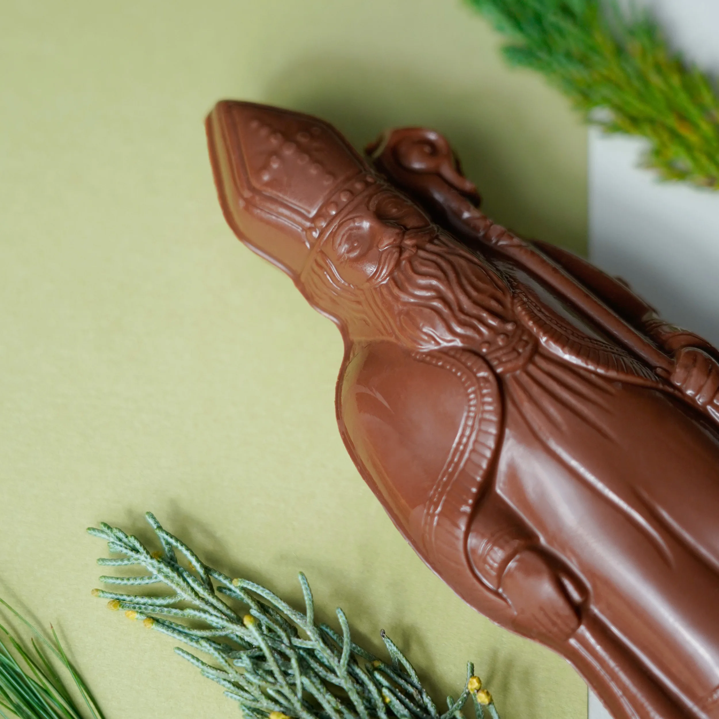 Nikolaus aus Milchschokolade liegt schrägt im Bild auf grünem Untergrund eingerahmt in Tannenzweige